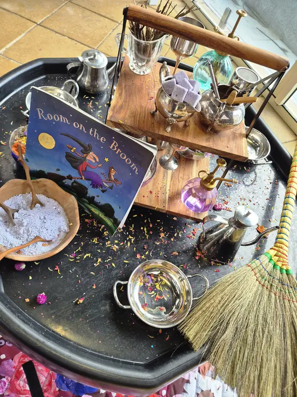 Potion-making tray themed on the picture book Room on the Broom, with silver teapots, jugs, scented powder, dried petals and a broom.
